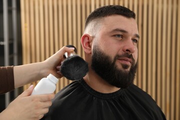 Fototapeta premium Hairstylist applying talcum powder with brush onto man's beard at salon, closeup