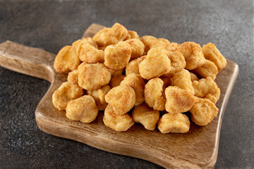 Golden crispy chicken popcorn on wooden cutting board against a gray background. Close-up. Fast food