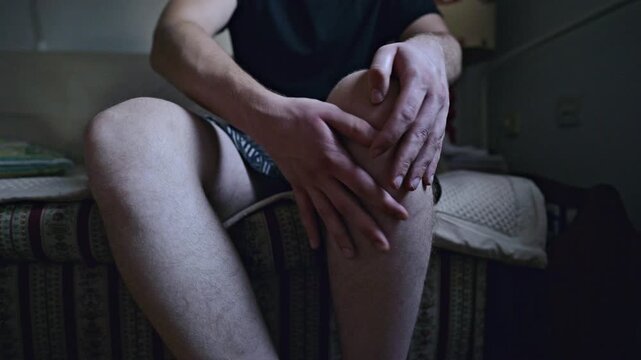 A person sits and gently massages their painful knee, indicating an injury or discomfort in the joint. The focused action suggests an attempt to alleviate the aching pain and soothe the area.
