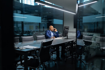 Mature African American businessman talking on cellphone in spacious office meeting room. Confident executive handling corporate discussions with calm professionalism