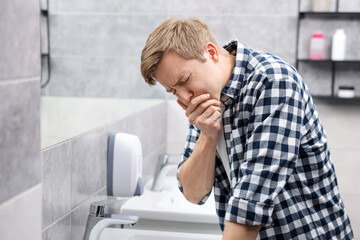 Young man suffering from nausea over sink in bathroom