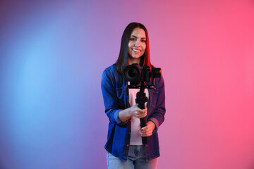 Videographer filming on camera using gimbal stabilizer against background with color lights. Space for text