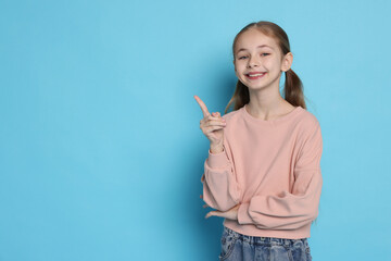 Portrait of cute girl on light blue background, space for text