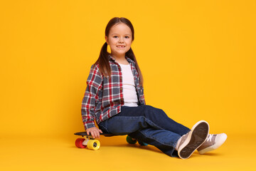 Cute little girl with penny board on orange background