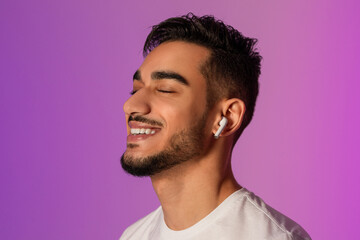 A handsome young Arab man is enjoying his favorite music while wearing earphones. He closes his eyes in a serene moment, surrounded by soothing neon light. It is a perfect evening to unwind.