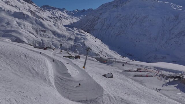 Andermatt Ski Resort in Switzerland. People Tourists riding skiing Snowboarding on snow-covered Slope, Aerial Drone View