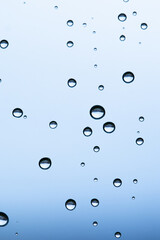 Macro shot of water droplets on a window with a serene light-blue sky backdrop on a rainy day.
