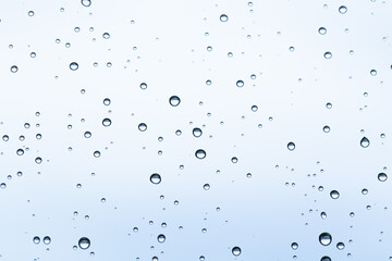 Macro shot of water droplets on a window with a serene light-blue sky backdrop on a rainy day.