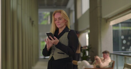 Businesswoman holding phone to ear while talking on a call in office hallway, smiling and walking during informal conversation