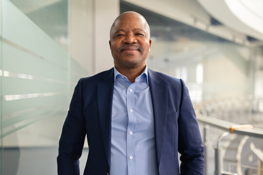 Mature African American businessman standing confidently in a modern building. Professional executive with a friendly smile, reflecting leadership and stability