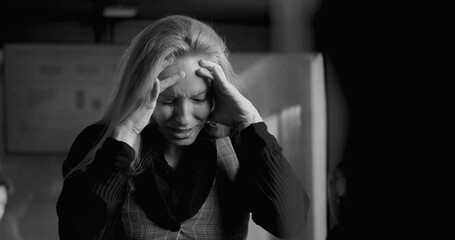 Businesswoman in black and white photo holding head in hands, overwhelmed by stress during intense...
