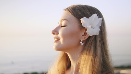 Woman with flower in hair enjoying sunset by the sea, radiating tranquility and blissful serenity in a coastal setting at dusk