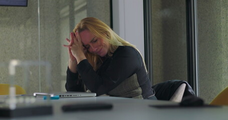 Business woman resting head on arms while seated at desk, appearing mentally drained and emotionally withdrawn in quiet office environment