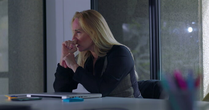 Business woman seated with hand to forehead, overwhelmed by work pressure and fatigue during intense moment of stress in quiet modern office