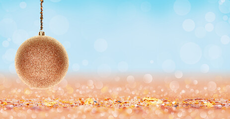Banner of Golden glitter Christmas bauble hanging above a sparkling sandy surface with soft bokeh...