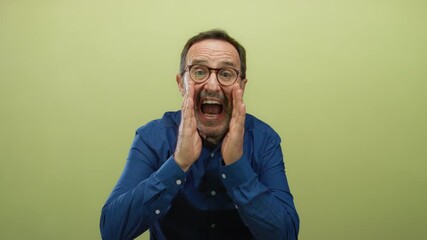 Senior man gestures passionately on an isolated yellow background wearing glasses and blue shirt