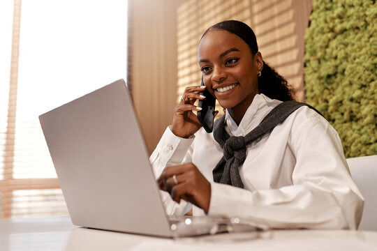 African American businesswoman multitasking on phone and laptop at office desk