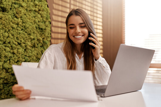 Woman having a phone call while working on laptop in modern office