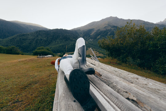 Person mountains meadow wooden relax outdoor lying on a rustic log bench in alpine field, traveler resting with boots and jacket, peaceful nature escape and wide scenic view. - Powered by Adobe