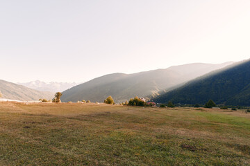 Fototapeta premium Meadow valley mountains at sunrise over an open field with dry grass and rolling hills, panoramic landscape with soft morning light and distant peaks in peaceful rural scenery.