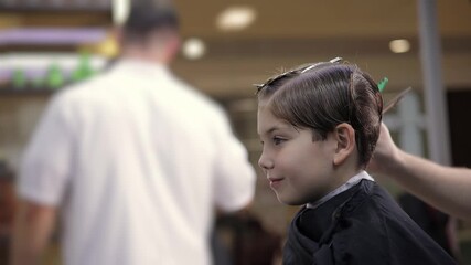 Young caucasian boy receiving haircut at salon barbershop with male barber in background.