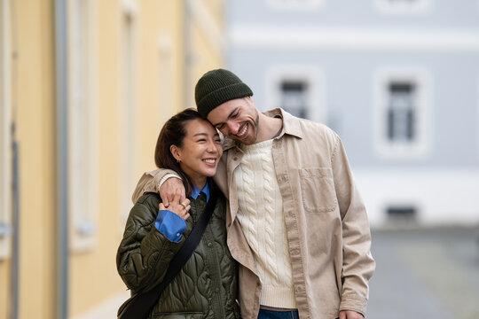 Happy multiracial couple embracing while walking on city street