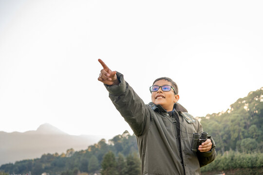 Young boy in glasses pointing and holding binoculars, exploring nature, adventure concepts - Powered by Adobe