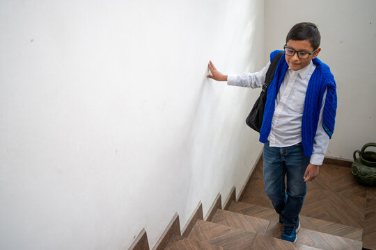 Mexican boy student with backpack and glasses walking down stairs in school building - Powered by Adobe