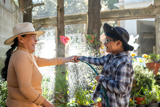 Mexican grandmother and boy laughing while playing with water hose in garden