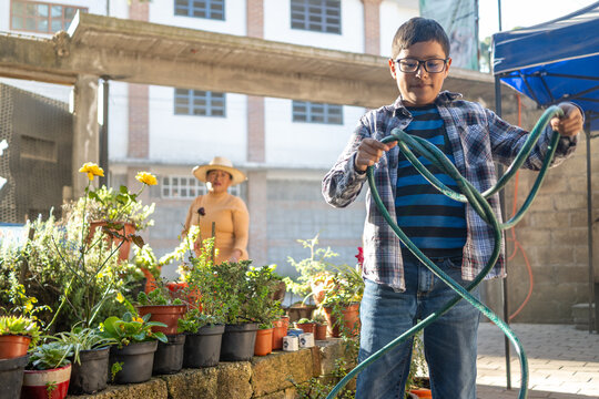 Mexican boy holding a hose, helping with gardening alongside grandmother