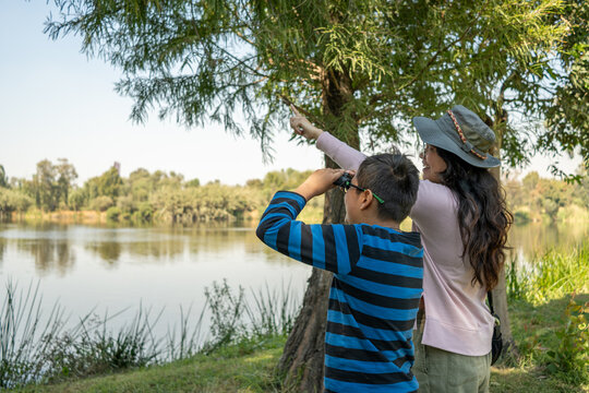 Mother and son birdwatching by lake pointing at nature during family outing - Powered by Adobe