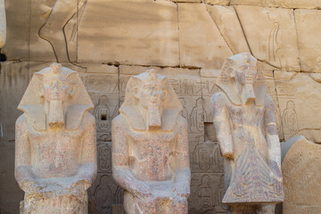 Egypt, Luxor, 01.02.2022.Ancient Egyptian stone statues standing and seated among sandstone temple ruins with carved hieroglyphs and warm light, Karnak temple.