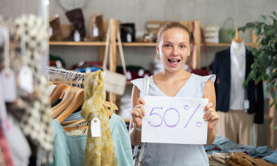 Portrait of teen girl holding sign saying 50 percent discount in clothing store
