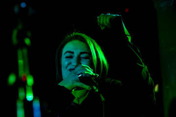 Young caucasian female singing on stage under green spotlight