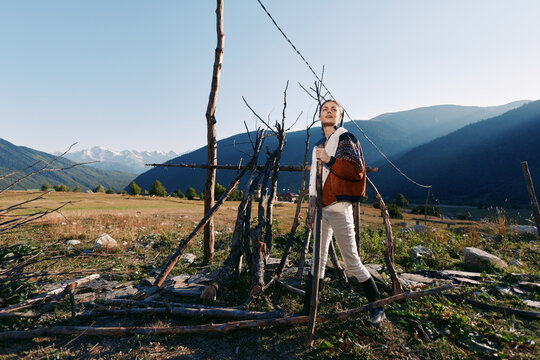 Woman hiking with backpack in mountain meadow, standing near rustic wooden fence, enjoying nature and outdoors travel, scenic landscape with distant peaks and clear blue sky.