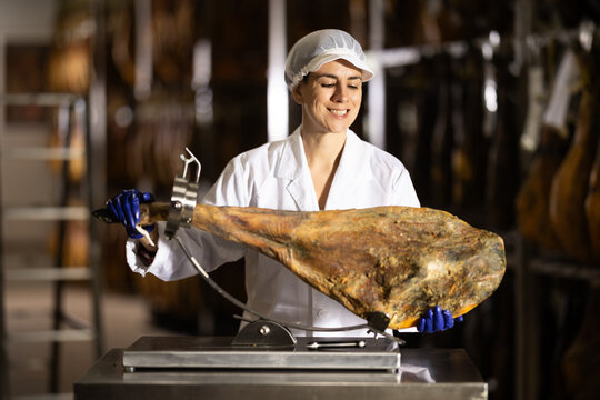 Qualified female specialist works in a meat factory, she has put the ham on a stand and is preparing to slice it. Process of making jamon