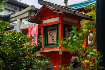 A vermilion lantern with kanji stands before stone torii and red banners in Kyoto, Fushimi Inari...