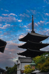 Obraz premium Yasaka Pagoda at Hokan ji Temple stands above rooftops in Higashiyama, Kyoto, at dusk. Stacked eaves, a tall finial, greenery, and a copper lantern add detail.