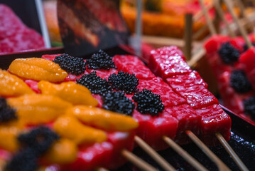 Close up skewers show red tuna cubes with black roe and orange uni at a Kyoto stall, likely Nishiki...