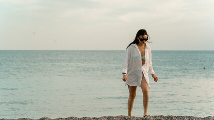 Beautiful woman walking back from the sea on a scenic pebble beach. Serene atmosphere, natural beauty, and peaceful coastal moment. Perfect for travel and lifestyle themes.