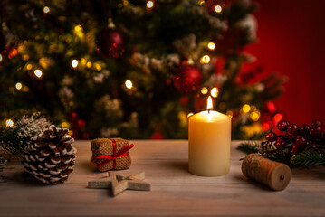 Lit candle surrounded by pinecones, tiny gifts and festive decor creating a warm Christmas atmosphere with blurred tree lights in the background