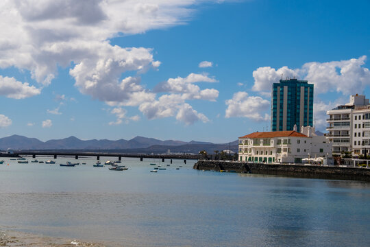 Arrecife Lanzarote waterfront view featuring historical buildings and people leisurely walking along the promenade. The serene atmosphere and clear sky create a picturesque scene