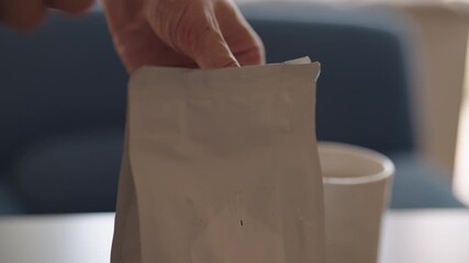 Close-up of human hand opening coffee bag and reaching for instant coffee with golden scoop, emphasizingthe daily routine of preparing comforting warm drink for breakfast. Shooting in slow motion. - Powered by Adobe