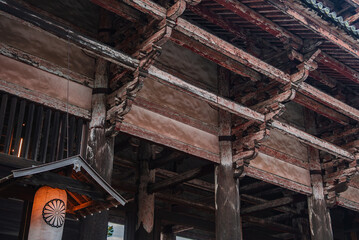 Close up shows wooden beams, bracket supports, and a glowing lantern with chrysanthemum crest at a...