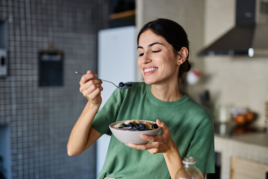 Portrait of a young woman preparing and eating breakfast, drinking juice in the kitchen at home