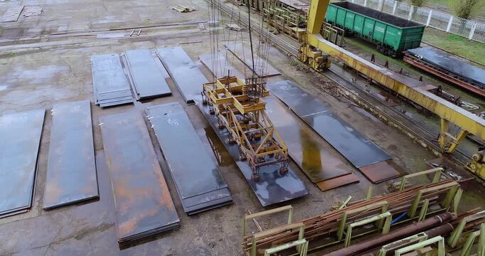 Electromagnetic crane moving metal sheets in steel yard. Gantry crane lifting steel sheets with electromagnet in metal warehouse. Storage of metal sheets in outdoor warehouse. Rolled Metal warehouse