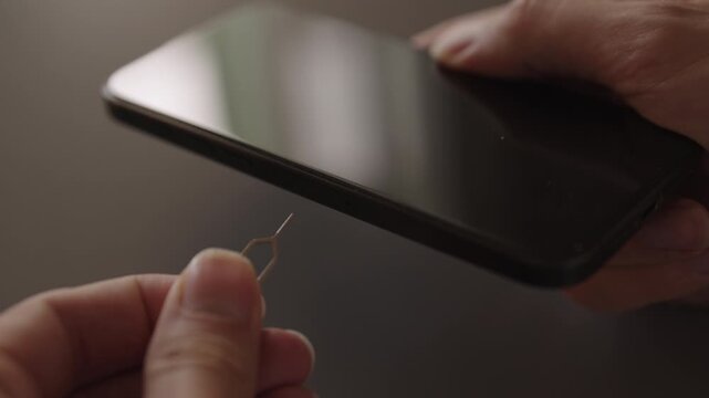Close-up of male hands inserting sim ejector tool into smartphone to remove or replace subscriber identity module, signifying mobile phone maintenance, upgrade, data transfer, slow motion.