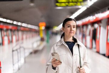 Girl with phone stand at subway stop, underground station platform, waiting for transport and...