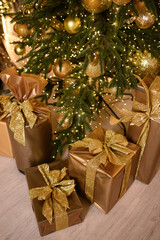 Close-up of beautifully wrapped golden Christmas gifts under a festive tree decorated with sparkling gold ornaments and warm lights.