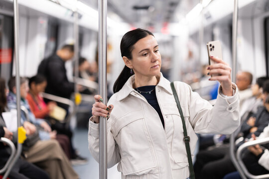 In the subway car, woman with a mobile phone makes a selfie or scans QR code